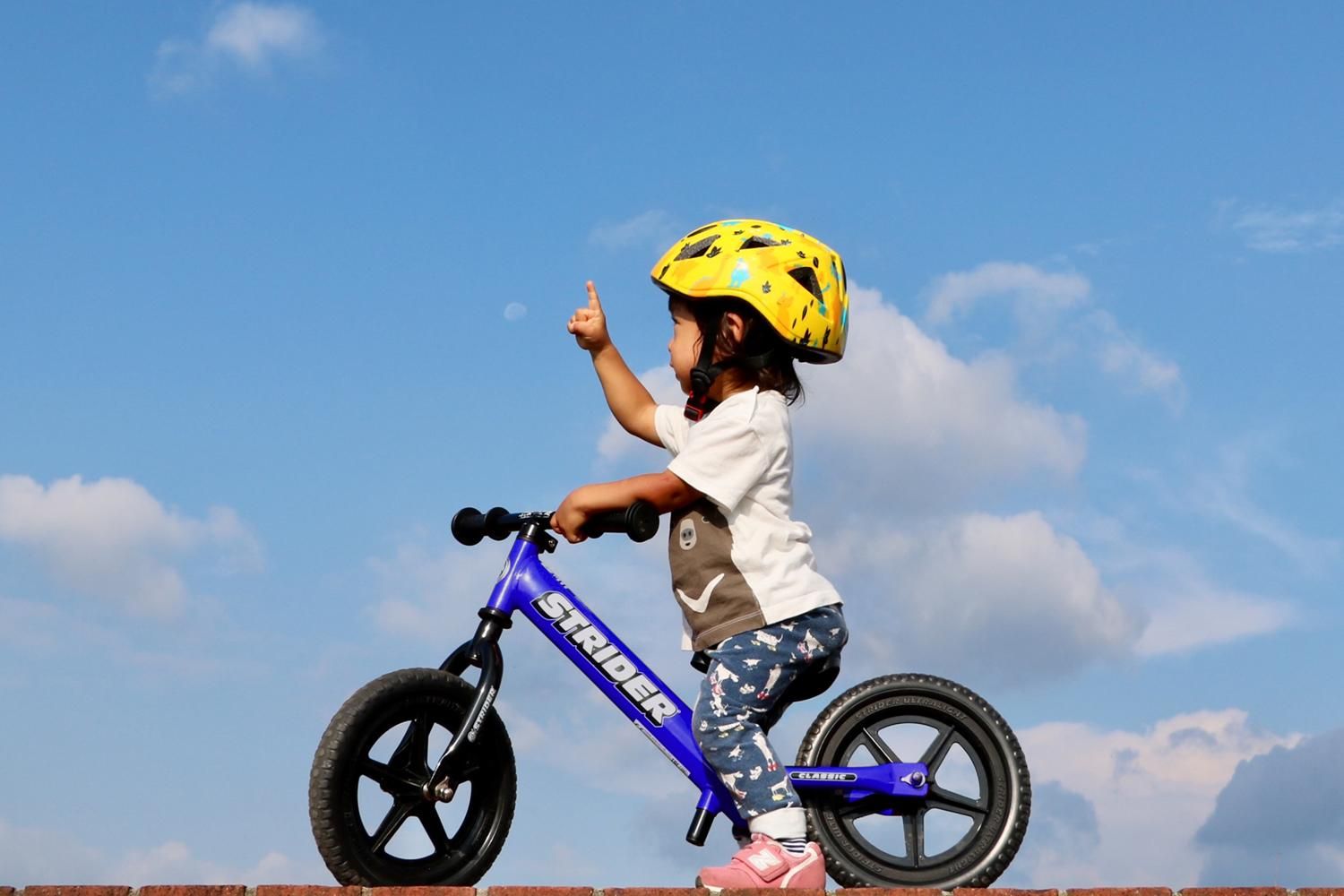 A girl on a blue Strider 12 Classic points to the sky during a ride