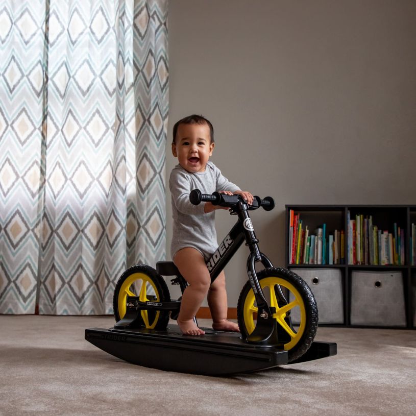 A baby laughs while playing on a Strider 12 Sport 2-in-1 Rocking Bike with yellow Ultralight Wheels