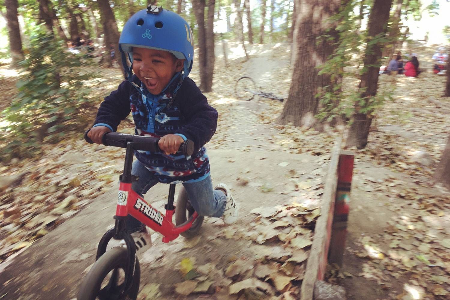 A boy rides a red Strider balance bike through the woods