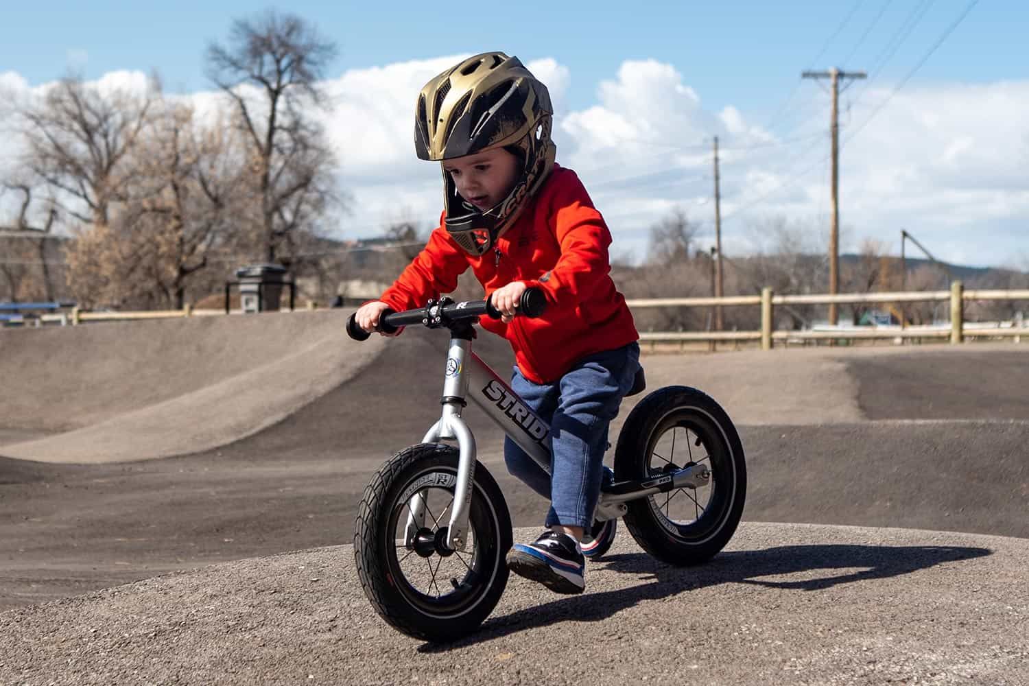 A child rides a silver Strider 12 Pro balance bike with ST-R Carbon Fiber wheels in a bike park